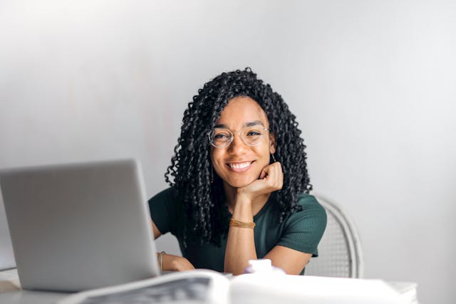 person with glasses smiling in front of a grey laptop